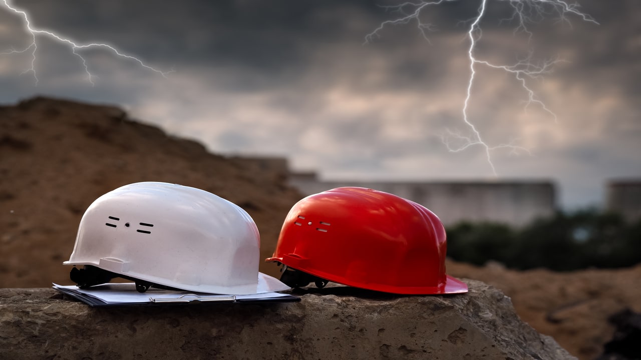 Dois capacetes de obras em destaque e ao fundo uma tempestade.