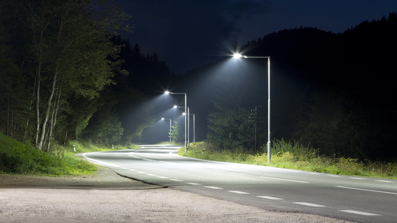 Uma rodovia a noite, sendo iluminada por postes de luz.