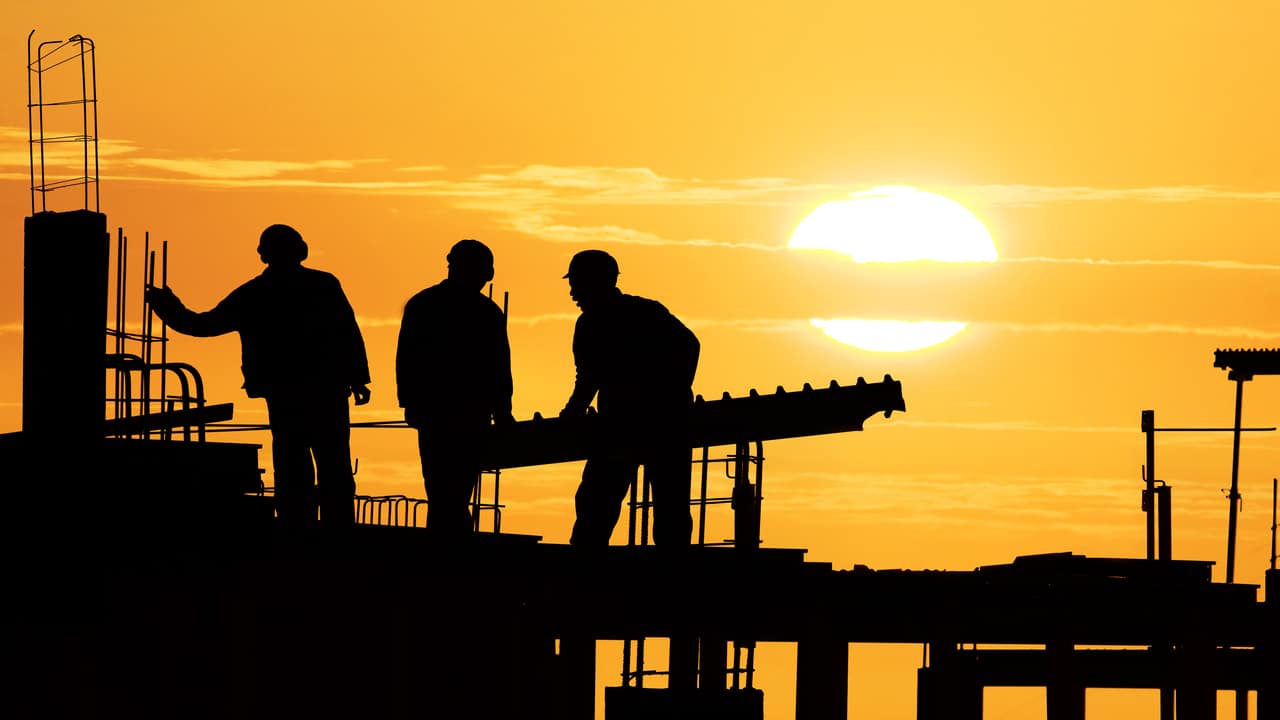 Sombra de homens trabalhando em uma obra ao pôr do sol.