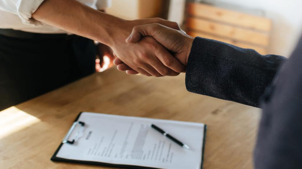 Homens se cumprimentando e um contrato acima de uma mesa.