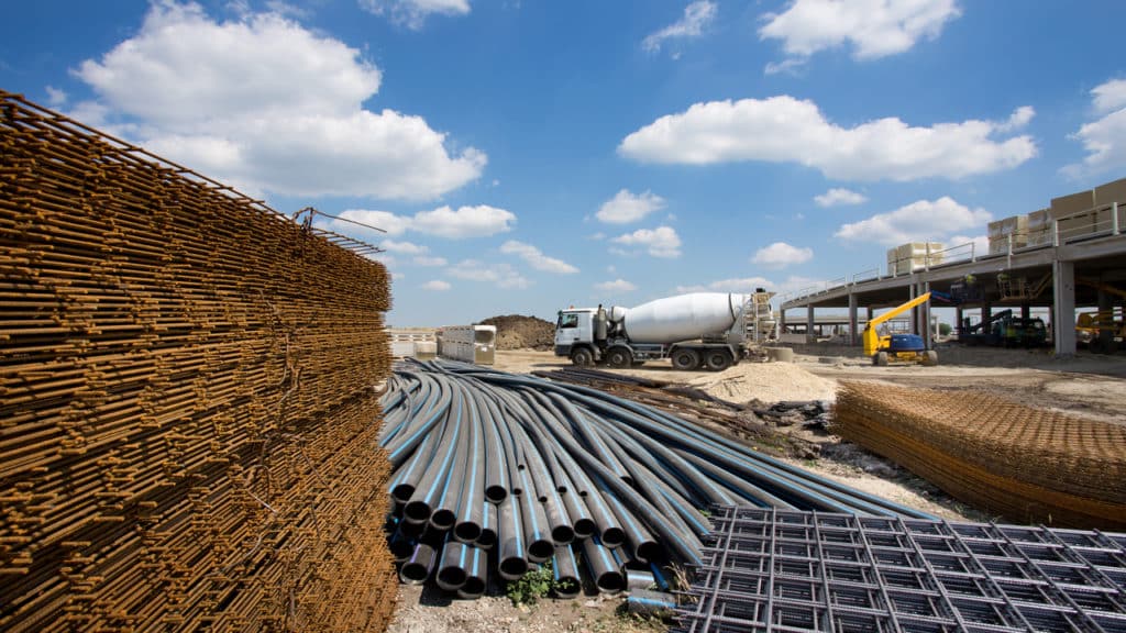 Vários materiais de construção e uma betoneira atrás em uma área aberta.