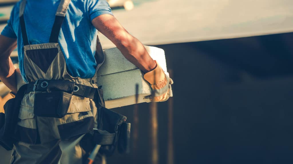 Homem que trabalha em uma obra, segurando alguns blocos de concreto.