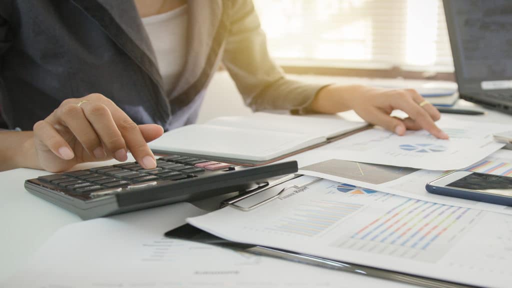 Mulher fazendo o planejando de suas finanças, mexendo em uma calculadora com algumas planilhas na mesa.