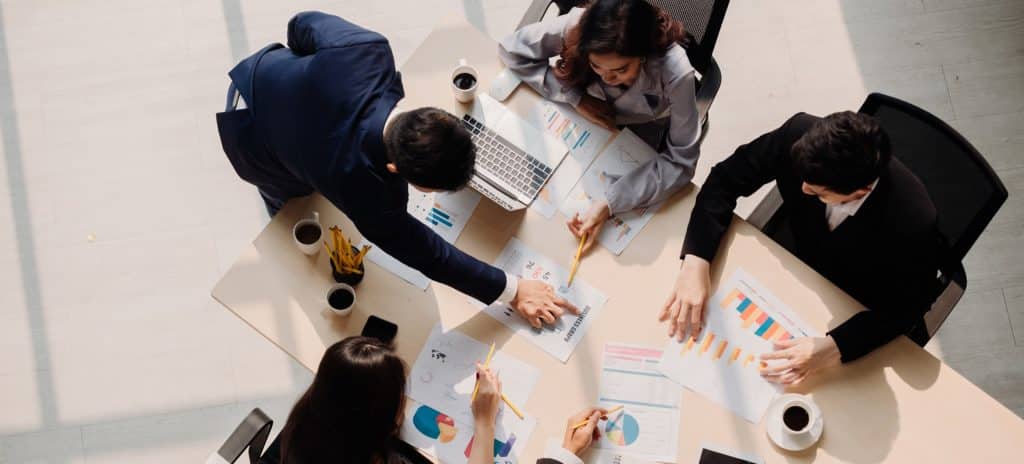 Cinco pessoas em reunião analisando gráficos e resultados