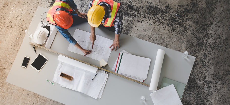 Engenheiros vistos de cima, eles estão examinando projetos espalhados sobre uma mesa que detalham a participação da empresa em eventos, uma das maneiras de anunciar para construtoras